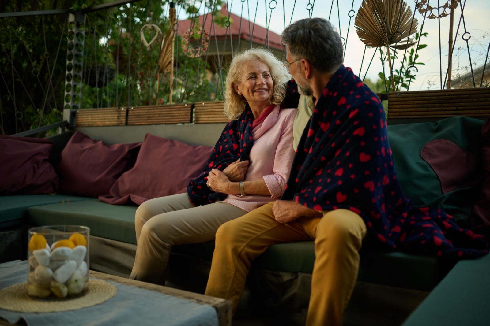 Una pareja mayor bajo una manta en la terraza de una casa, al final de la temporada